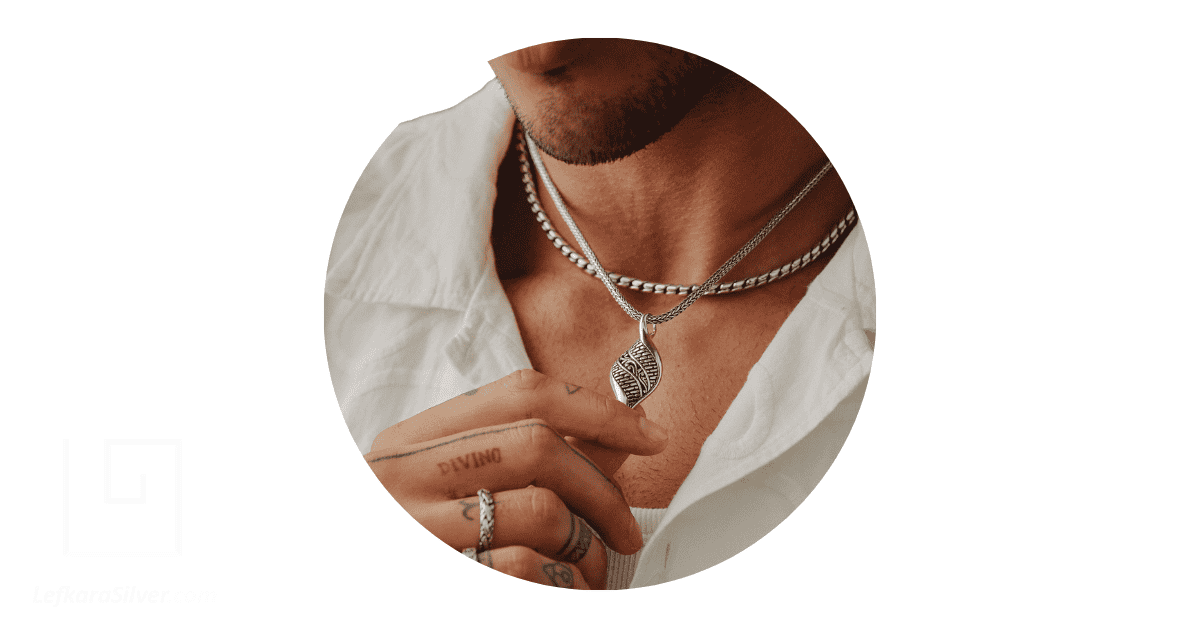 A man holding the silver pendant of the silver necklace around his neck