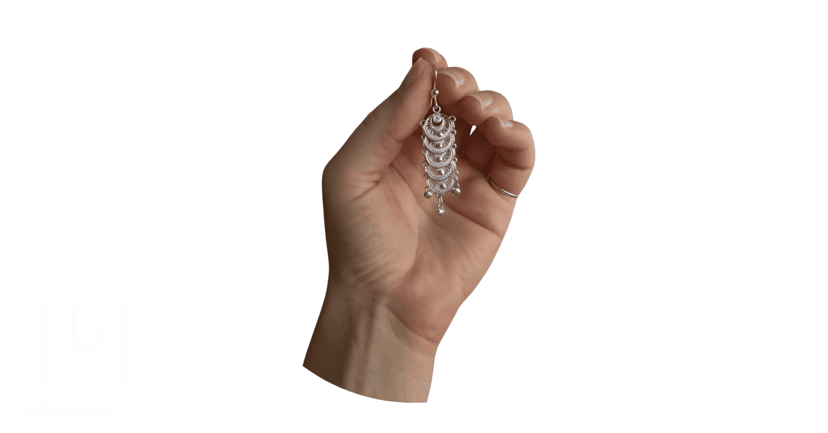 A hand holding a silver filigree earring depicting Cyprus jewellery