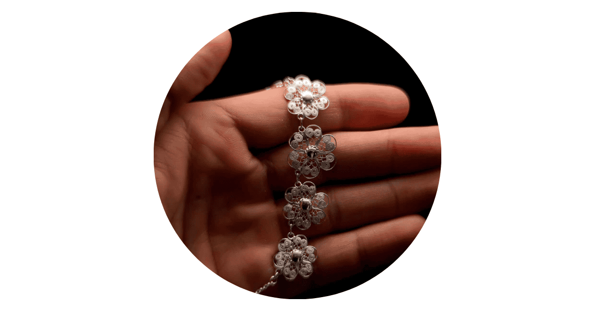 a had holding a silver filigree necklace