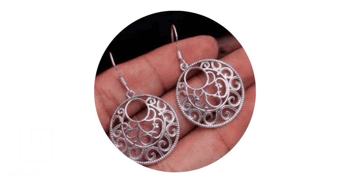 a person holding a pair of silver filigree earrings
