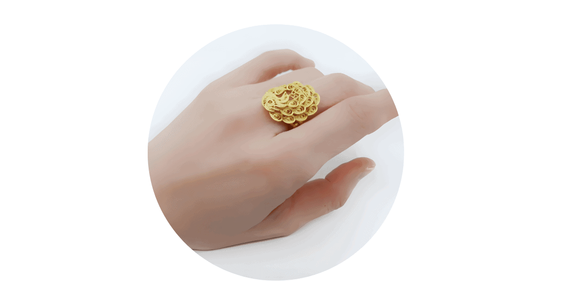 a person's hand with the middle finger adorned with a gold filigree ring.