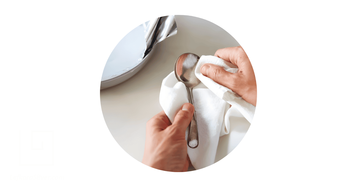 a person's hand cleaning a silver spoon. 