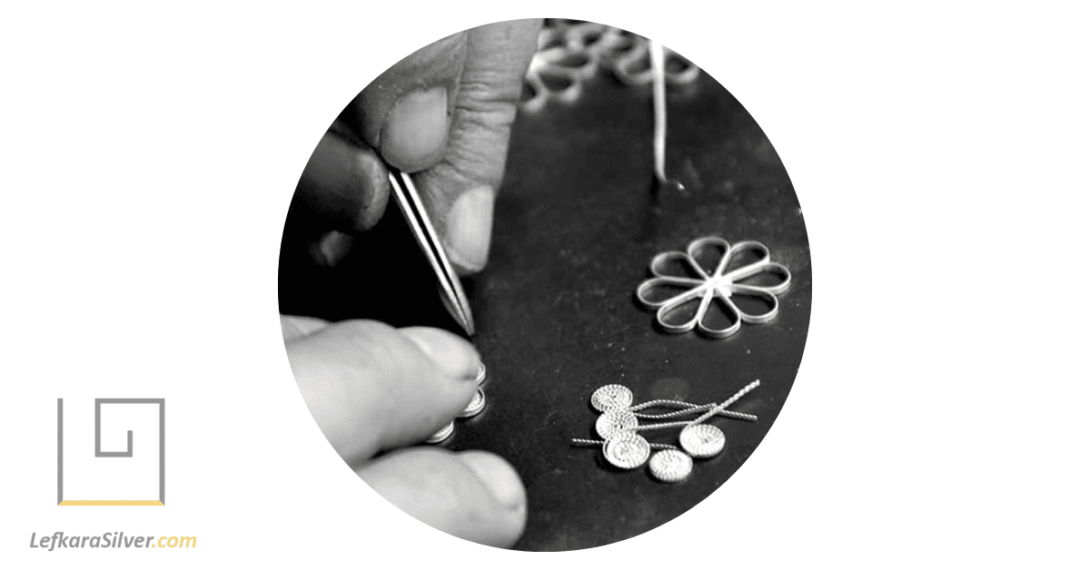 a person crafting a delicate, handmade wire-wrapped pendant necklace, showcasing the intricacy and detail of the piece against a black background.