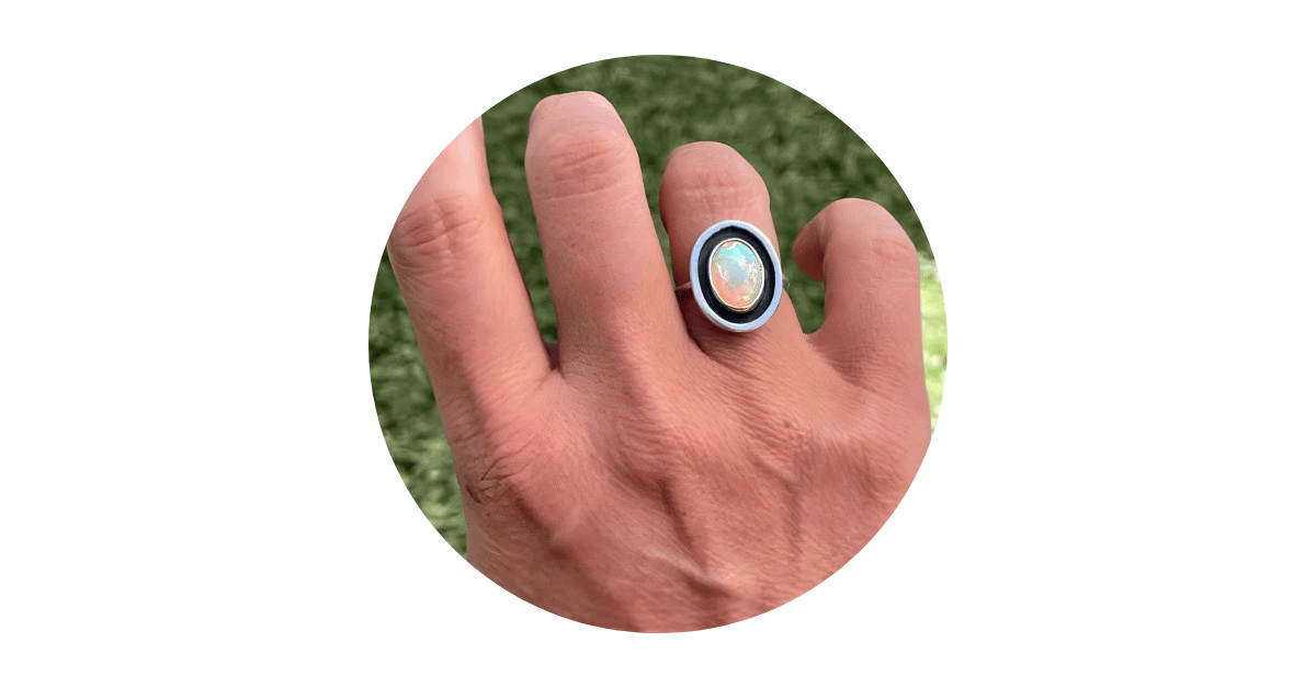 a man's finger adorned with an opal ring.