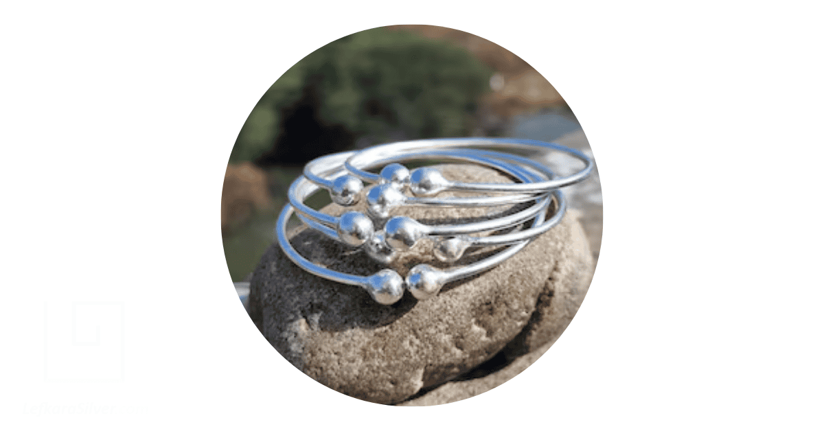 Silver bangles stacked on stone.