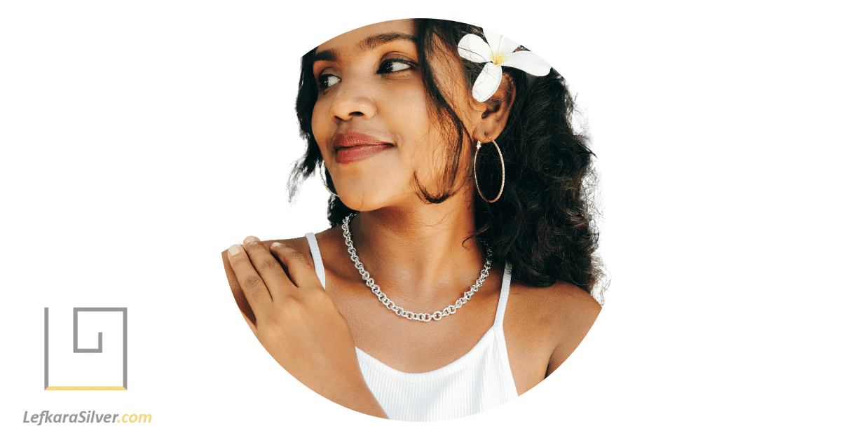 a woman smiling in the sunshine with a bold silver chain around her neck.
