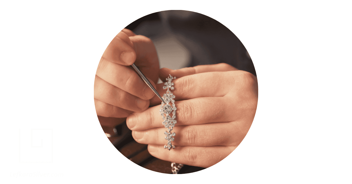hands holding a silver necklace and a tool used for jewelry crafting