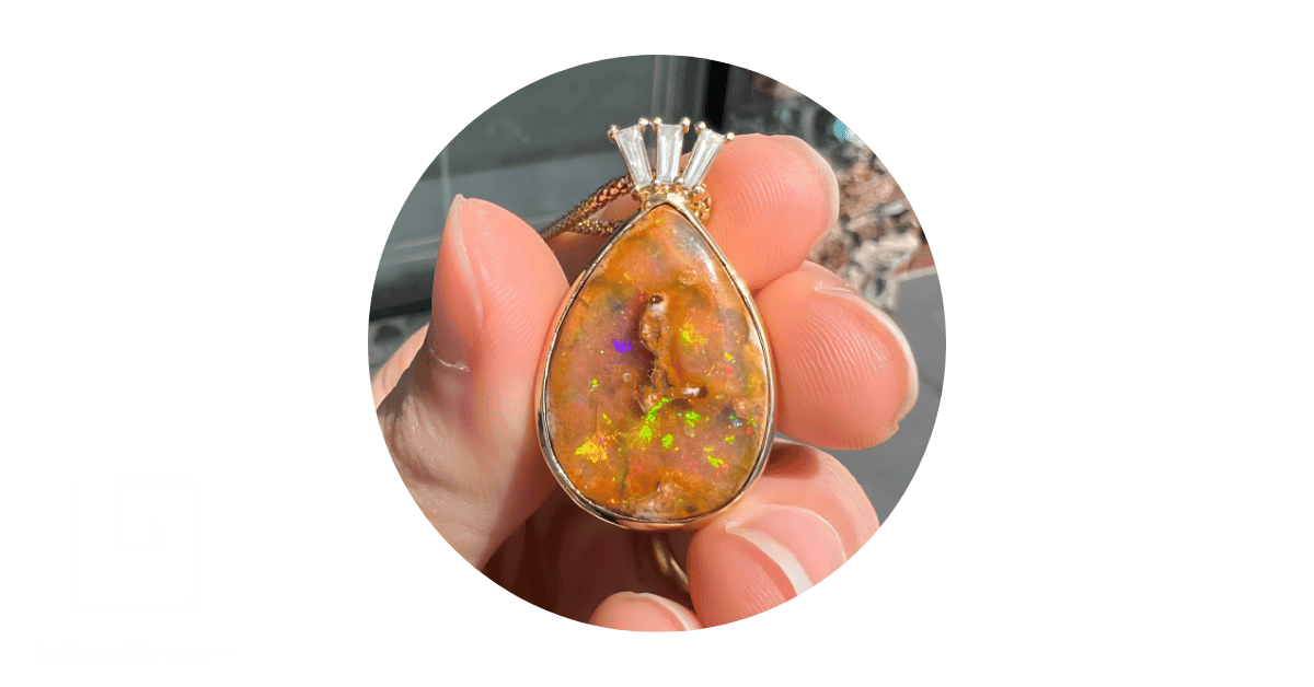 A person's hand holding a Mexican opal pendant.