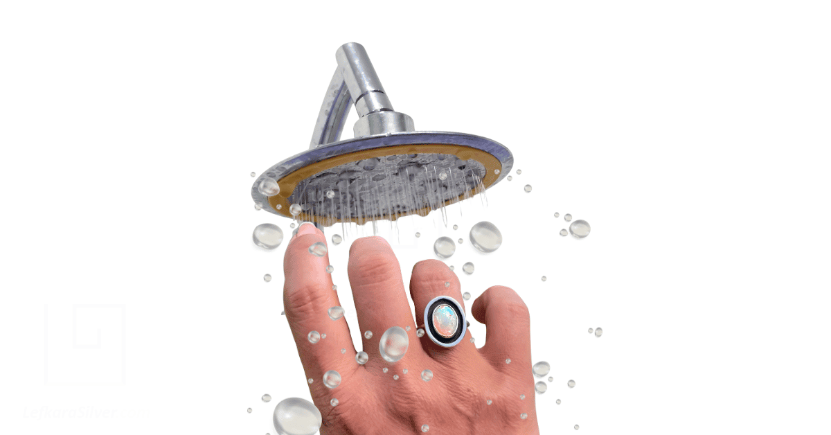 A person's hand with an opal ring under a shower head. with water bubbles.