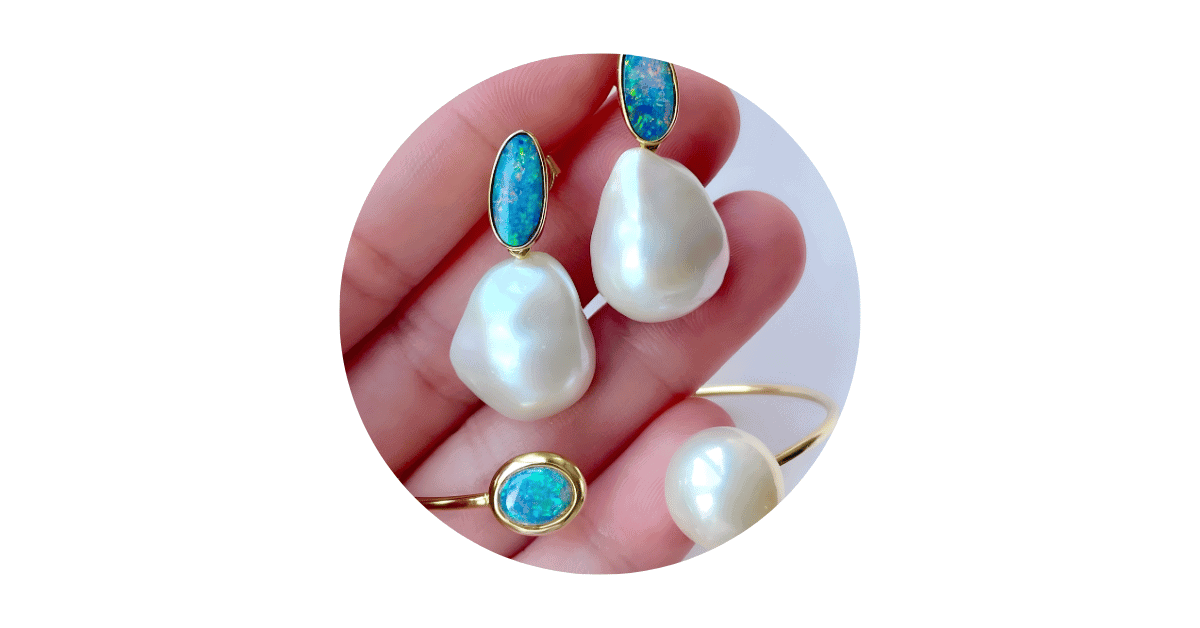 A person's hand holding an opal and pearl jewelry set. 