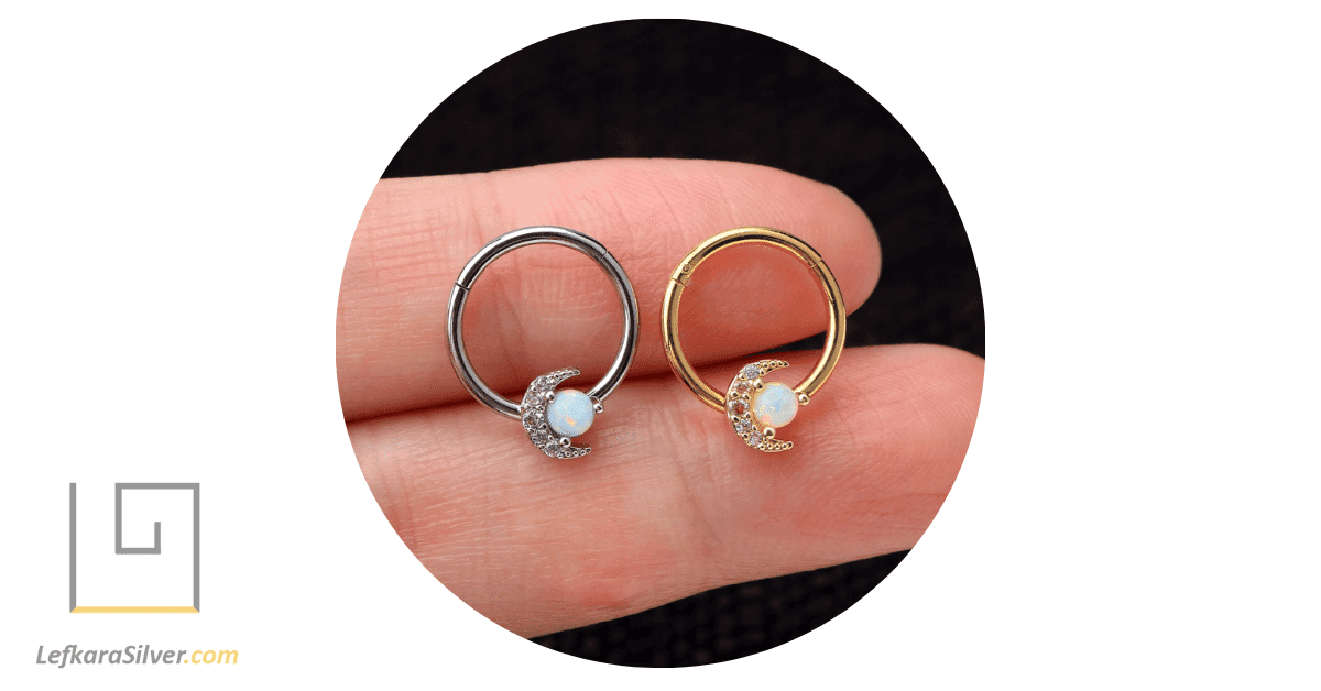 a person holding silver and gold opal daith earrings