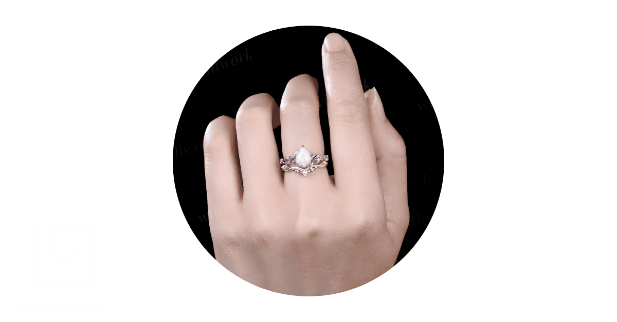 A person's hands with an opal and pearl engagement ring on their middle finger. 
