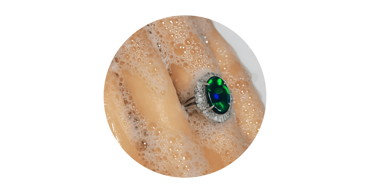 A person's soapy finger with an opal ring on.