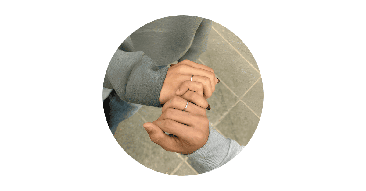 A couple's hands wearing matching promise rings, with their pinky fingers locked in a pinky promise.