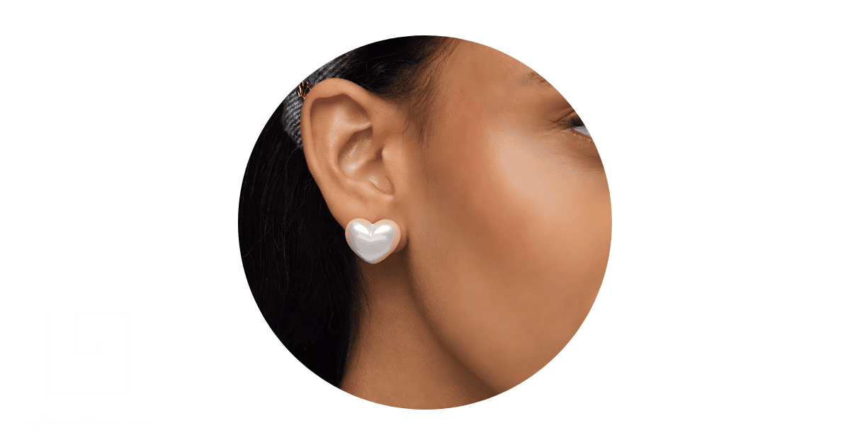 a person's ear adorned with heart-shaped pearl earrings.