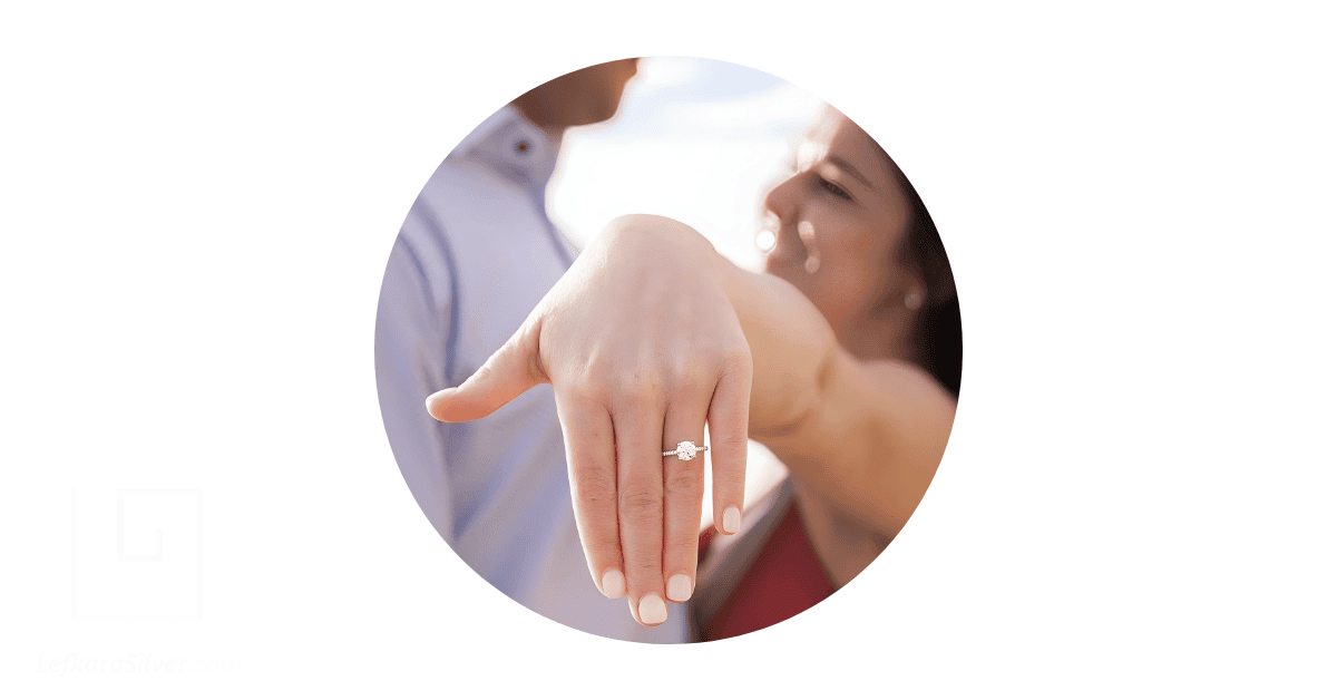 A couple posing for pictures, with the woman's outstretched hand adorned with an engagement ring on the finger.