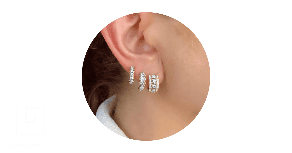 A person's ear adorned with multiple huggies diamond earrings. 