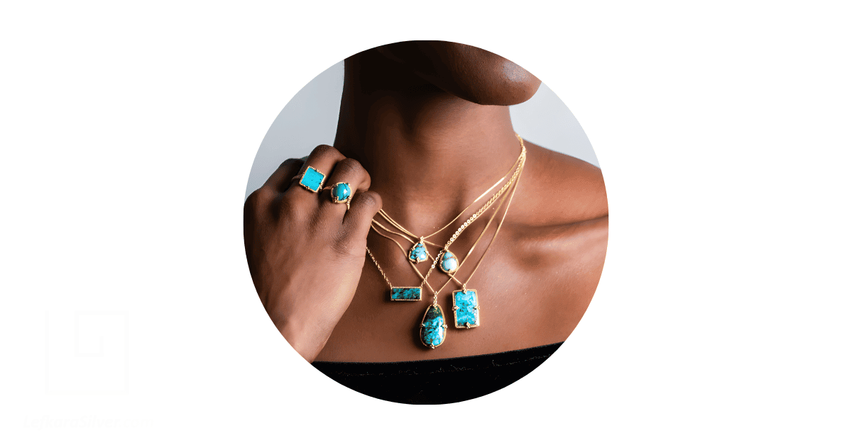 A person wearing a tack of turquoise necklace and rings.