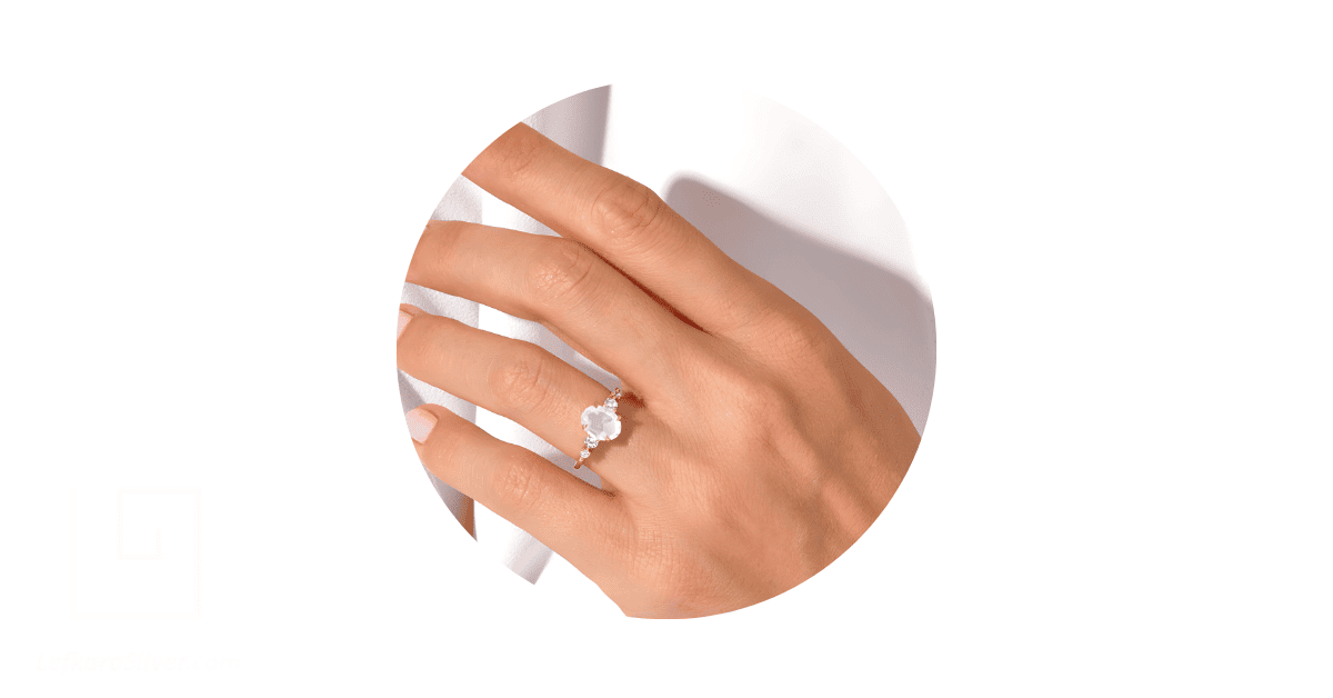a person's finger adorned with a moonstone engagement ring. 