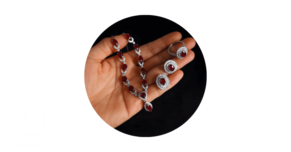 a person's hand holding a pigeon blood ruby jewelry set. 