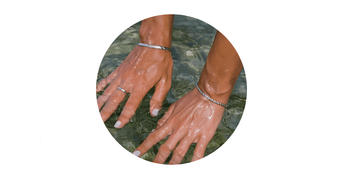 A person's hands adorned with silver bracelets and a .ring, and dipped in water.