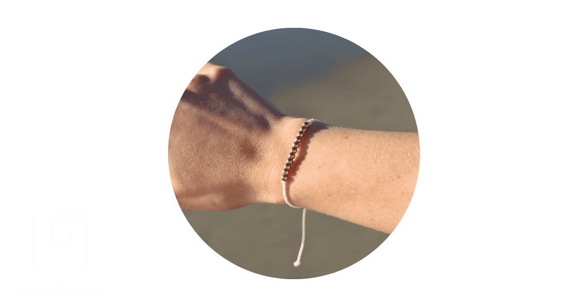 a person's wrist adorned with a bracelet made with strings and beads. 
