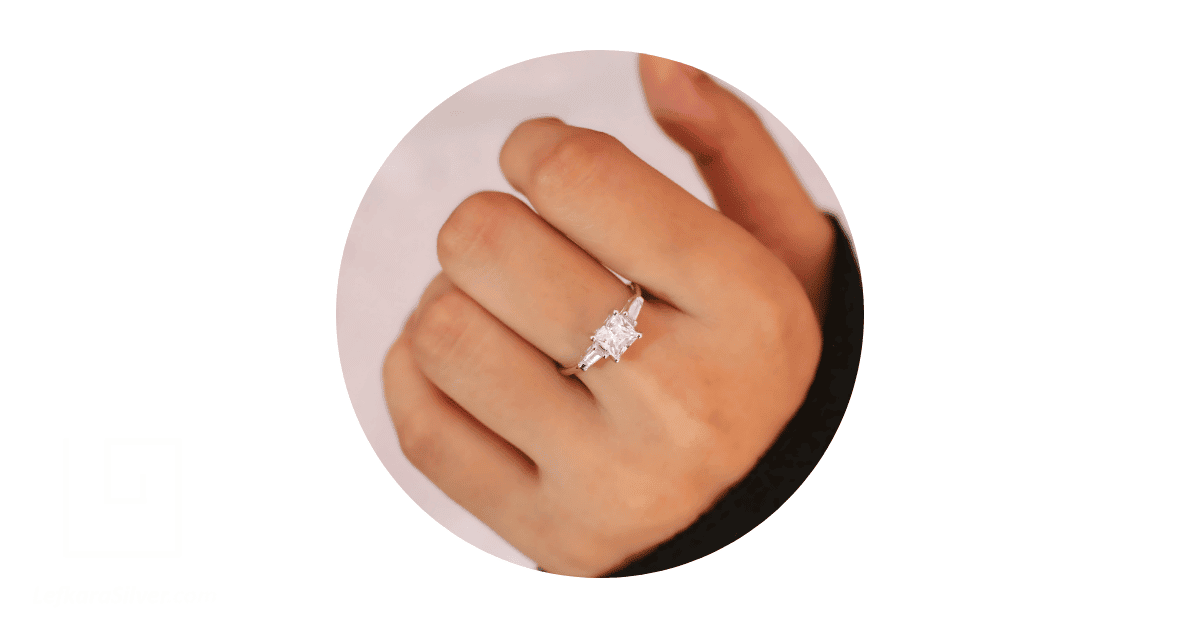 a person's finger adorned with a diamond engagement ring.