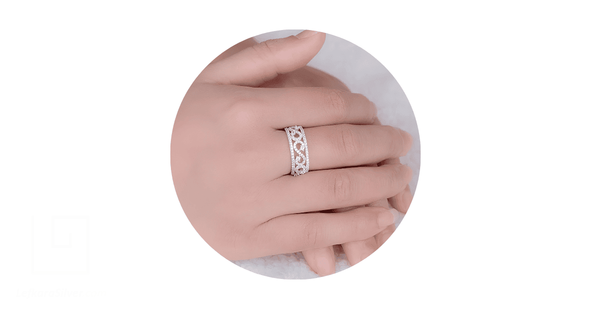 a person's finger adorned with a silver filigree wedding ring.