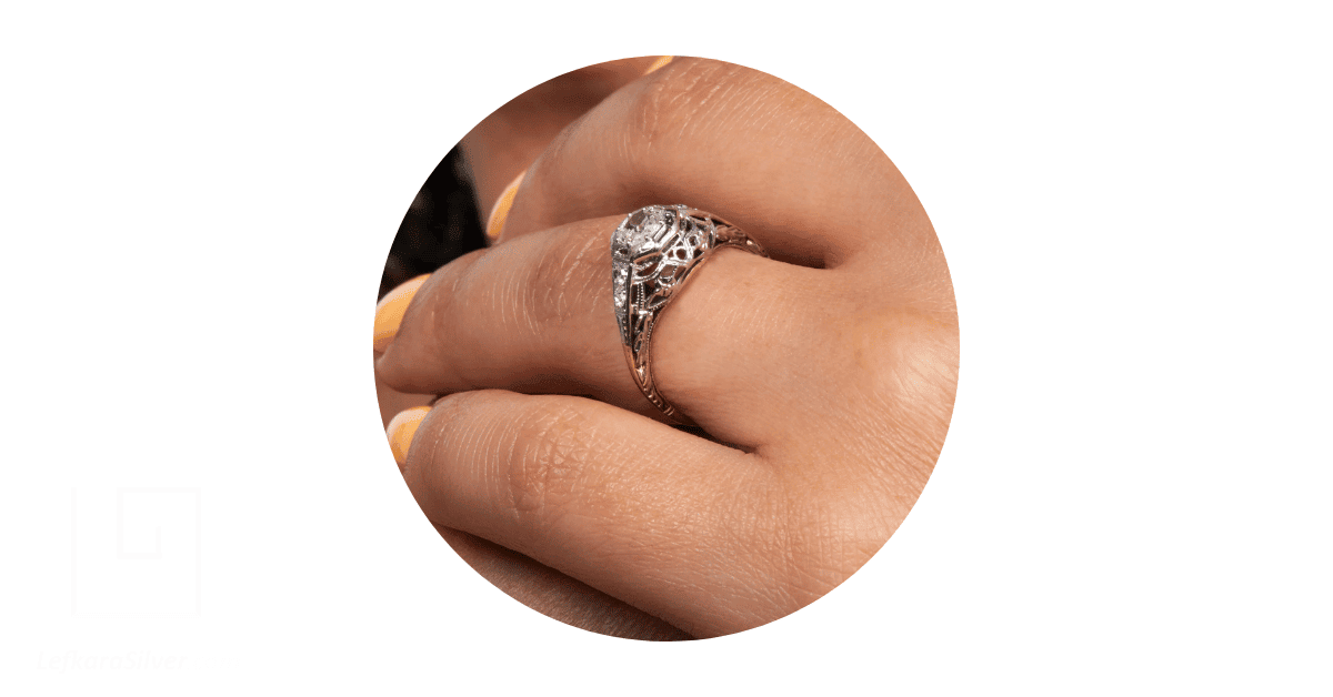 a person's finger adorned with a filigree wedding band.