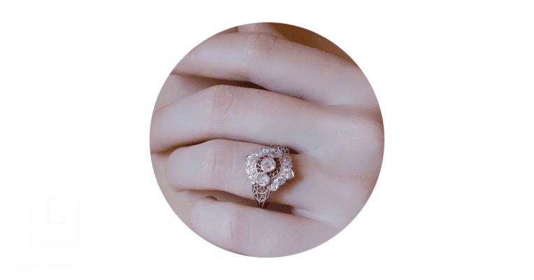 a woman's fingers with a silver filigree engagement ring sitting on the middle finger.