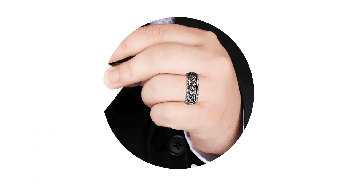 a man's finger adorned with a black filigree wedding band.