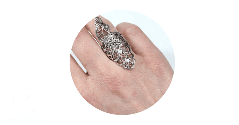 a person's finger adorned with a vintage filigree ring.