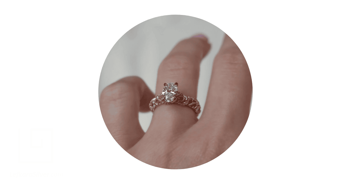 a person's finger adorned with a gold filigree engagement ring. 