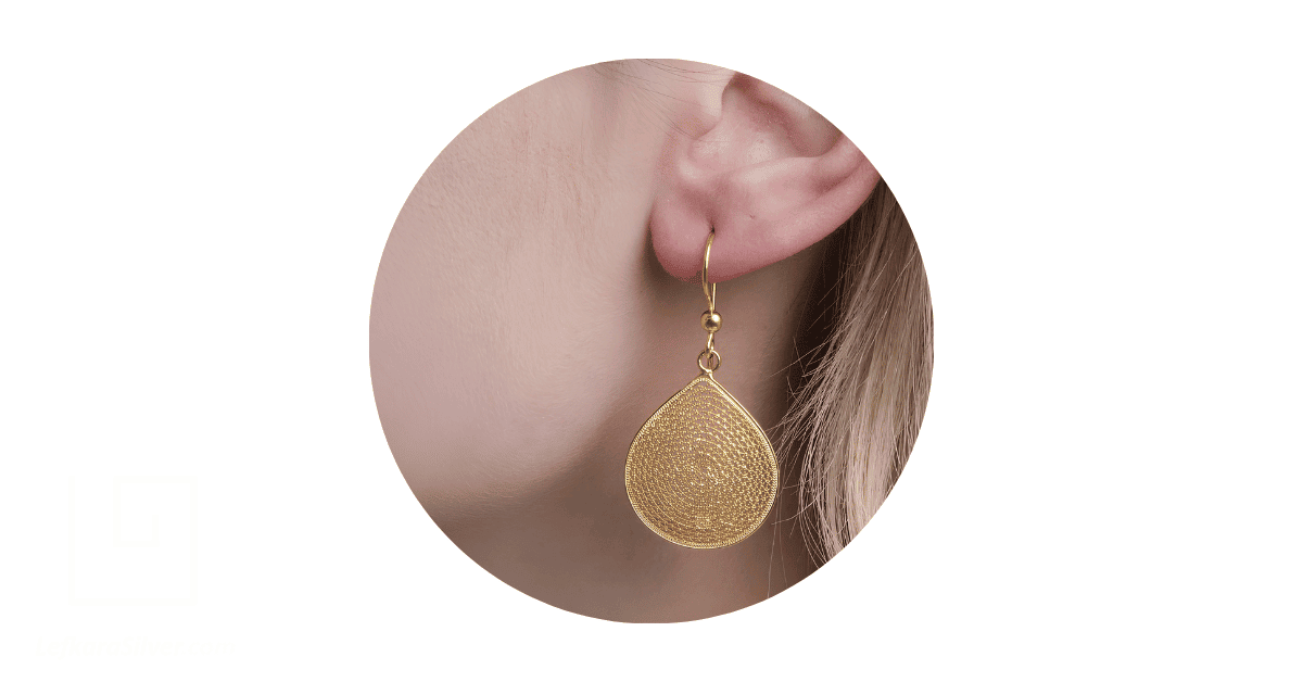 a person's ear adorned with a gold filigree drop earring.